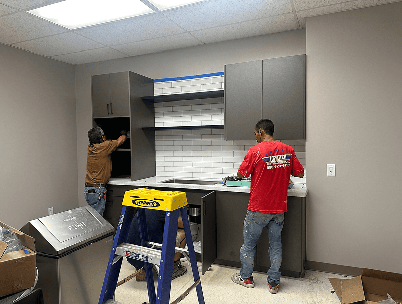 Workers installing cabinets in a kitchen area.